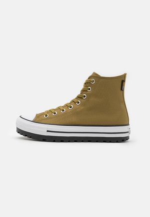 Hoher Sneaker aus olivgrünem Canvas mit weißer Gummisohle, schwarzen Streifen, Metallösen und strukturierter schwarzer Laufsohle, von der Seite gezeigt.