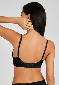 Bralette de encaje negro con tirantes delgados ajustables, cierre de gancho y ojal en la parte posterior, y una textura suave con patrones florales.