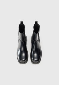 Bottes de cheville en cuir noir avec des panneaux élastiques sur les côtés et des languettes de tirage. Texture lisse, orteils ronds et semelle en caoutchouc épaisse.