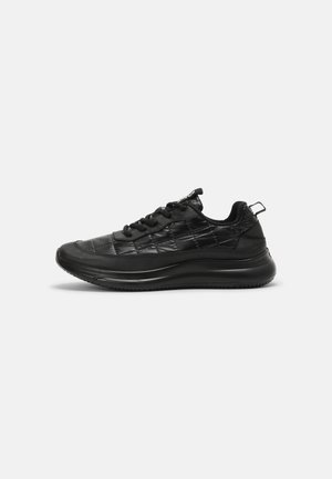 Czarny pikowany niski sneaker z grubą podeszwą, sznurowanym zapięciem i pętelką na pięcie, pokazany od zewnętrznej strony na białym tle.