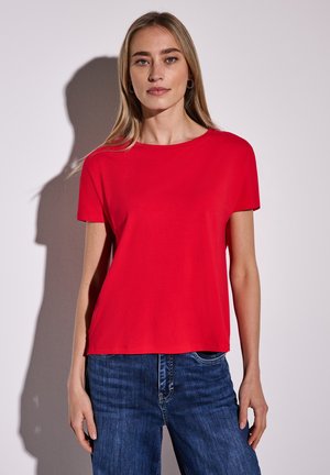T-shirt rossa a maniche corte in morbido cotone, con scollatura rotonda e vestibilità comoda, abbinata a jeans in denim blu.