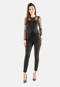 Top negro de manga larga con diseño de puntos transparentes y acentos de encaje, combinado con pantalones negros ajustados y zapatos de tacón.