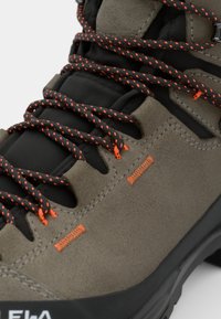 Szare zamszowe buty trekkingowe z czarnymi akcentami, teksturowana powierzchnia, pomarańczowe lanki i wzmocnione oczka dla większej wytrzymałości. Czarna gumowa podeszwa.