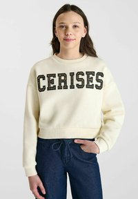 Crème-kleurige cropped sweatshirt met "CERISES" in zwarte en bruine blokletters, met een geribbelde halslijn en manchetten.