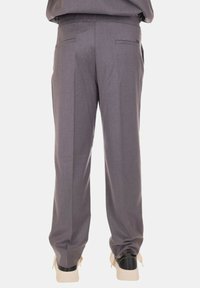 Pantaloni grigi su misura con una texture liscia, dotati di due tasche posteriori e un design a gamba dritta. Indossati con sneakers nere e beige.