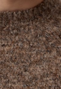Brązowa dzianina o teksturowanej powierzchni, zawierająca mieszankę jaśniejszych i ciemniejszych włókien, tworząca naturalny, organiczny wygląd.