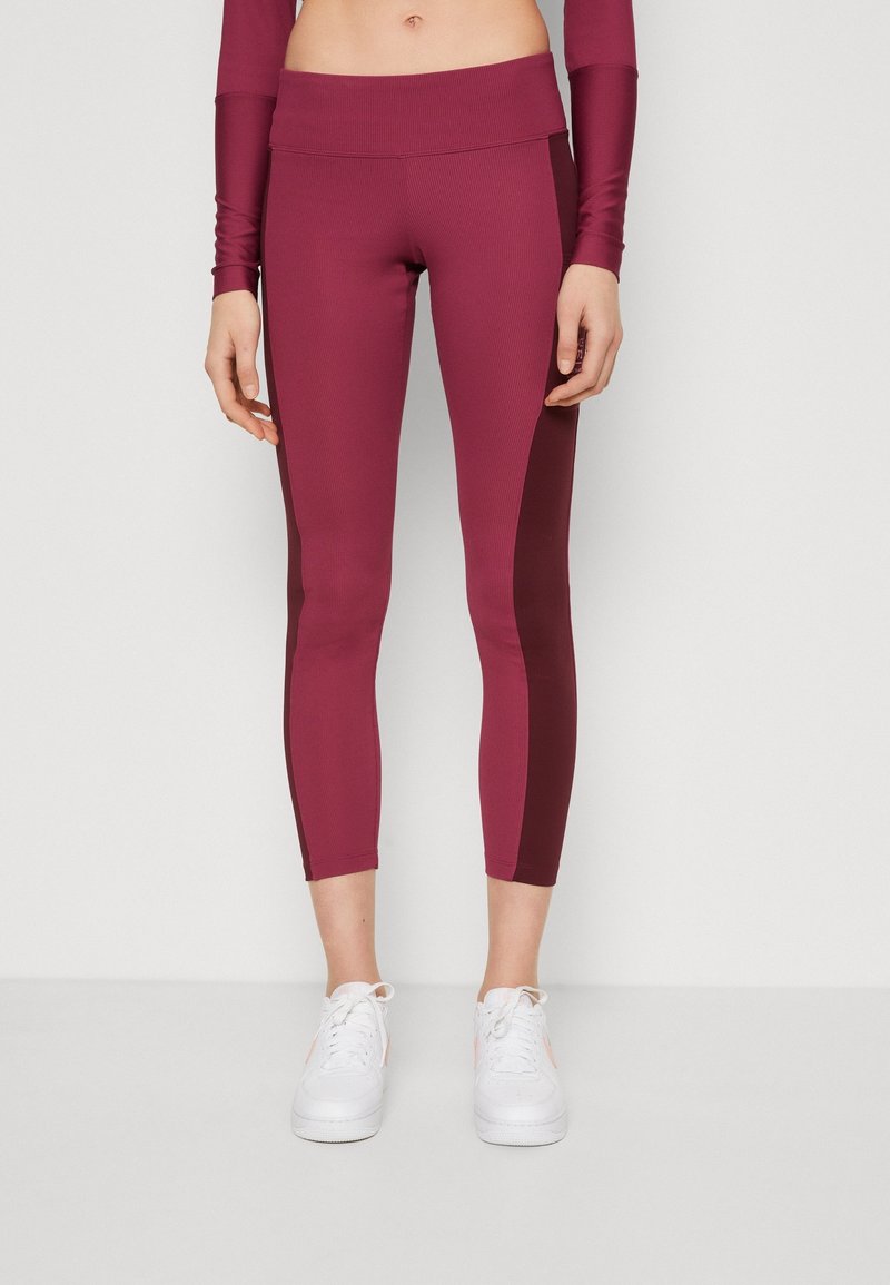 Vinröda leggings med ribbat mönster och kontrasterande paneler, med en hög midja som sitter ovanför höfterna. Bärs med vita sneakers.