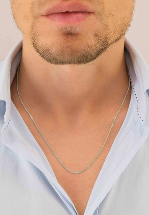 Collana in argento con una rifinitura fine e testurizzata, indossata sopra una camicia azzurro chiaro con colletto, che mette in risalto il suo design elegante sulla pelle.