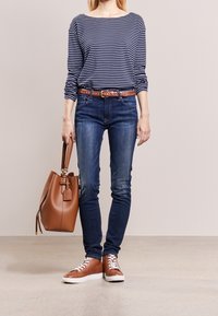 Gestreiftes navy- und weißes Langarmshirt, brauer gewebter Gürtel, dunkelblaue Skinny-Jeans, braune Leder-Sneaker und eine braune Tragetasche.
