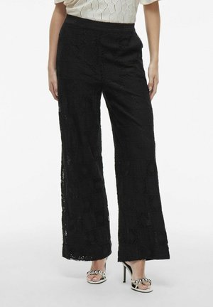 Pantaloni a gamba larga in pizzo nero con un motivo testurizzato, dotati di vita alta e fit fluido. Abbinati a sandali con tacco alto.