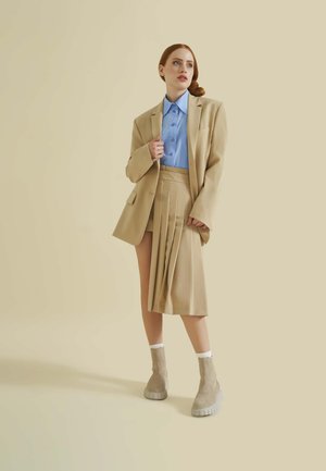 Beige oversized blazer over een lichtblauw overhemdd, gecombineerd met een geplooide beige rok en taupe platformlaarzen. Glad texturen overal.