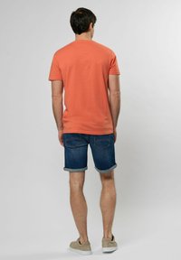 T-košile s krátkým rukávem v korálové barvě, vyrobená z měkké bavlny. V kombinaci s tmavě modrými džínovými šortkami s ohrnutým lemem. Neformální, lehké boty.