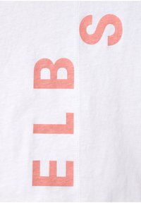Weißes Baumwoll-T-Shirt mit großen bedruckten Buchstaben in sanftem Pink. Glatte Textur mit sichtbaren Nähten an der Seite.