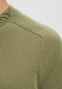 Oliivroheline kudumisi sweater, millel on ümmargune kaelus, sile tekstuur ja peened õmblusdetailid õlgadel.