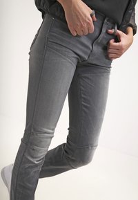 Šedé denimové džíny s úzkým střihem, které mají prošité detaily a středně vysoký pas. Materiál má hladkou texturu a mírnou elasticitu.