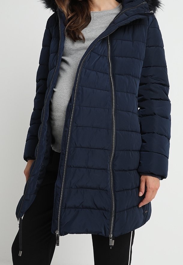 Navyblå puffjacka med en huva prydd med päls, kviltat mönster och dragkedja fram. Har sidfickor och kontrasterande dragkedja.