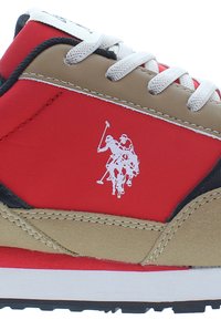 Červené tenisky s béžovými akcenty, obsahující logo, texturovaný materiál, bílé tkaničky a černou gumovou podešev. Je zde patrný sportovní design.