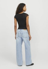 Top corto nero a maniche corte con dettagli trasparenti abbinato a jeans a gamba larga blu chiaro. Caratterizzato da due tasche posteriori e una vestibilità rilassata.
