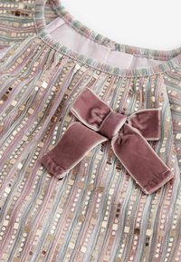 Gros plan de l'encolure de la robe avec des rayures multicolores et des sequins brillants, avec un grand nœud en velours mauve doux au centre.