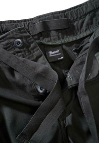 Črne hlače iz blaga z gladko teksturo, z gumbnim zapiranjem, nastavljivim pasom in etiketo, ki označuje velikost M in znamko.