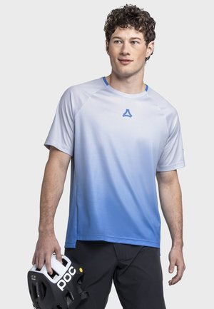 Junger Mann trägt ein blaues, verlaufendes Kurzarmhemd und hält einen schwarz-weißen Fahrradhelm, dabei blickt er leicht zur Seite.