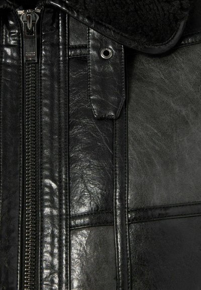 Chaqueta de cuero negro con cierre de cremallera, superficie texturizada y cuello de borreguillo con botones a presión y acentos de metal.