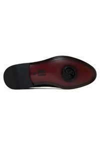 Semelle de chaussure en cuir noir avec une forme arrondie, dotée d'une semelle intérieure bordeaux et d'un détail logo en relief. Semelle extérieure en caoutchouc texturé pour une meilleure adhérence.