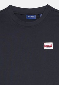 Marineblå bomulds T-shirt med rund halsudskæring. Har en lille rektangulær stofmærke med rød og hvid tekst. Glat tekstur, afslappet design.