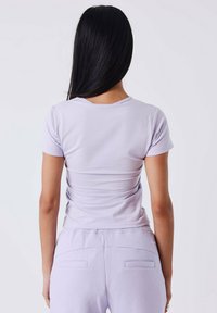 Camiseta ajustada de color lila con mangas cortas, tejido suave, escote redondo y un diseño ceñido al cuerpo, combinada con pantalones de chándal lila a juego.