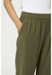 Pantalons en tissu léger couleur vert olive avec une taille élastique et des poches latérales ; coupe décontractée avec une texture douce et un tombé subtil.