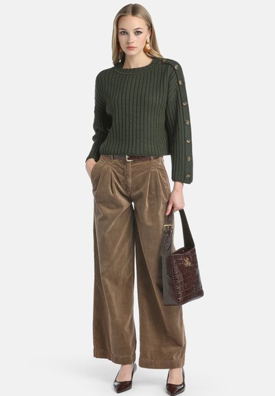Groen geribbelde trui met knoopaccenten, gecombineerd met een bruine corduroy broek met wijde pijpen. Accessoires zijn een donkerbruine tas met krokodillenpatroon.