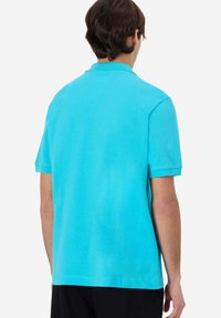 Polo shirt turchese a maniche corte in cotone, con colletto classico, di colore uniforme e una texture liscia con dettagli minimi.