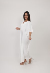 Robe maxi blanche et légère à manches courtes et décolleté en V, avec une coupe ample. Portée avec des sandales à talons transparents.