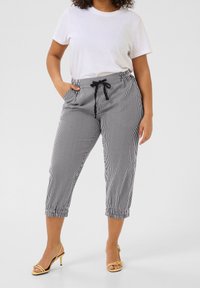 Pantalons capri à rayures noires et blanches, avec une taille élastique, un cordon de serrage ajustable et des poignets élastiques. Portés avec un t-shirt blanc uni.