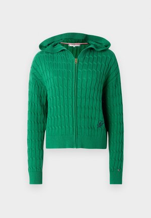 Grønn glidelåshette laget av teksturert strikket stoff. Har hette, ribbestrikkede mansjetter og hem, samt en logo på fronten.