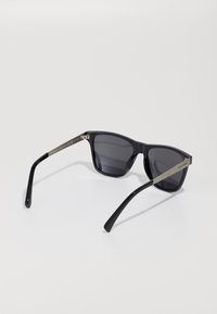 Black rectangular sunglasses with dark lenses and silver temple arms, resting open on a white surface.