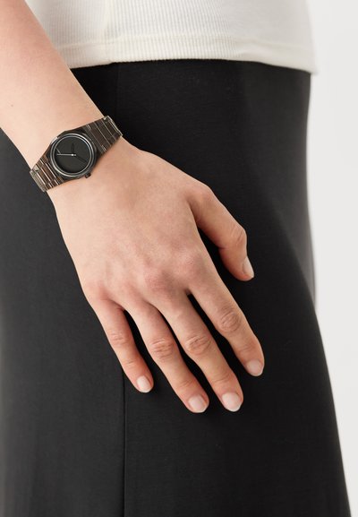 Black wristwatch with a round face and silver metal band. The watch features thin hour and minute hands against a black dial.