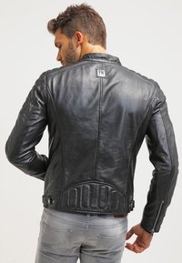 Chaqueta de cuero negra con un diseño ajustado, costuras de hombro elevadas, detalles acolchados en la espalda y acentos de cremallera en los puños y los lados.