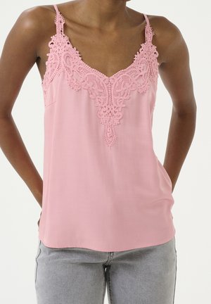 Lyserød silkecamisole med indviklet blonder langs halsudskæringen og tynde justerbare stropper. Kombineret med grå denim.