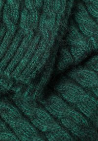 Grøn strikket stof med et tykt, struktureret ribmønster. Væven er fuzzy og viser en blanding af mørke og lyse grønne fibre.