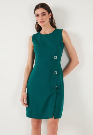 Sleeveless teal dress with a fitted design, featuring silver square buckle accents and a side slit for ease of movement. Smooth texture.