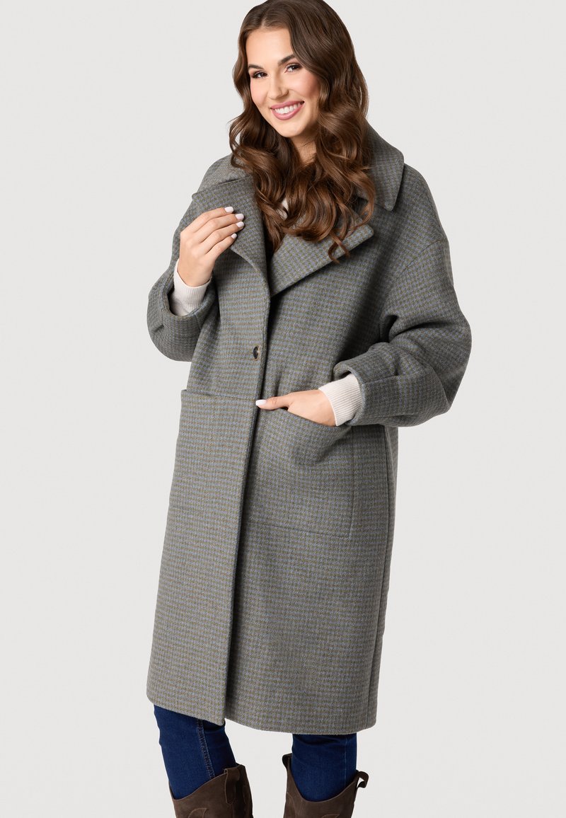 Sivý kabát s houndstooth vzorom, veľkým golierom, prednými vreckami a zapínaním na gombíky. Má jemnú textúru a nadrozmerný strih.