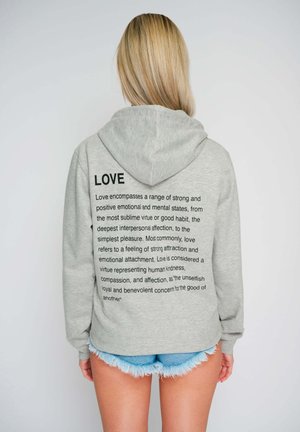 Hoodie gris avec cordon de serrage et texture douce, arborant un texte imprimé sur l'amour en lettres noires en gras dans le dos. Assorti à un short en denim.