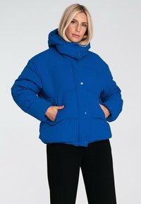 Niebieska kurtka puchowa z kapturem, o pudełkowym fasonie, z zapięciem na zatrzaski i bocznymi kieszeniami. Gładka struktura i pikowany wzór.