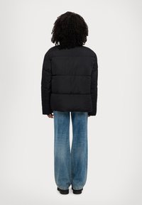 Doudoune noire avec une silhouette ample, dotée d'un design matelassé. Associée à un jean flare bleu clair et des chaussures noires.
