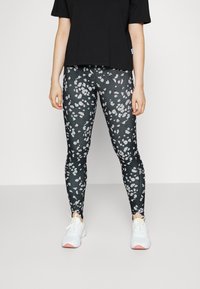 Leggings pretas com um padrão abstrato em branco e cinza, acompanhados por uma t-shirt larga preta e ténis brancos com sola rosa.