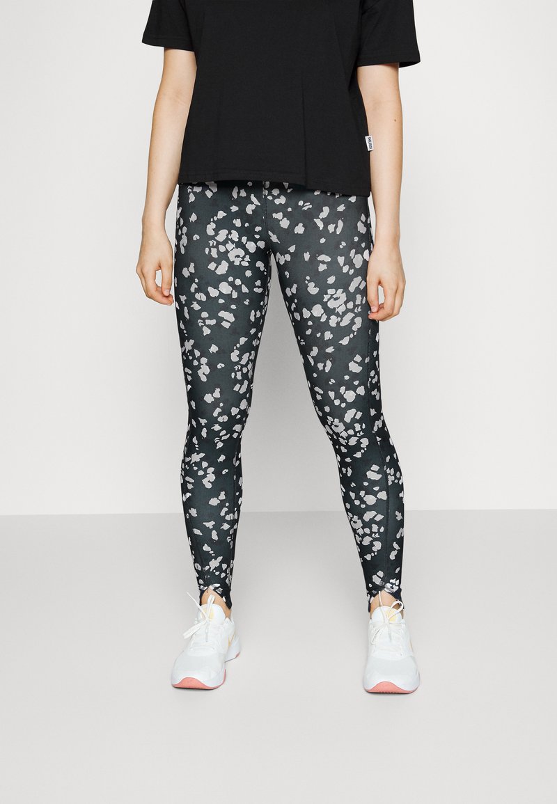 Leggings pretas com um padrão abstrato em branco e cinza, acompanhados por uma t-shirt larga preta e ténis brancos com sola rosa.