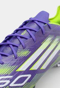 Purple soccer cleat with textured surface, features neon green accents and white stripes, and traditional lace-up design.