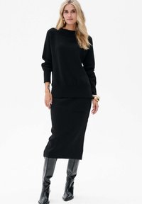 Czarny sweter dziani z szerokim dekoltem i długimi rękawami, w komplecie z czarną spódnicą kolanową z boczną kieszenią. Wysokie czarne botki.