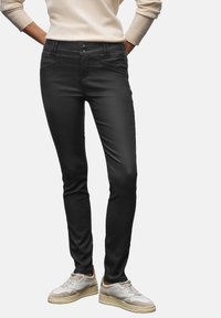 Pantalones de stretch negros con corte ajustado, que cuentan con dos bolsillos frontales, dos botones en la cintura y una textura suave. Llevados con zapatillas blancas.